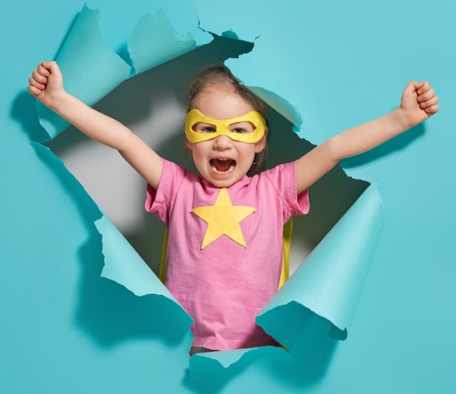 Little child playing superhero. Kid on the background of bright blue wall. Girl power concept. Yellow, pink and  turquoise colors.
