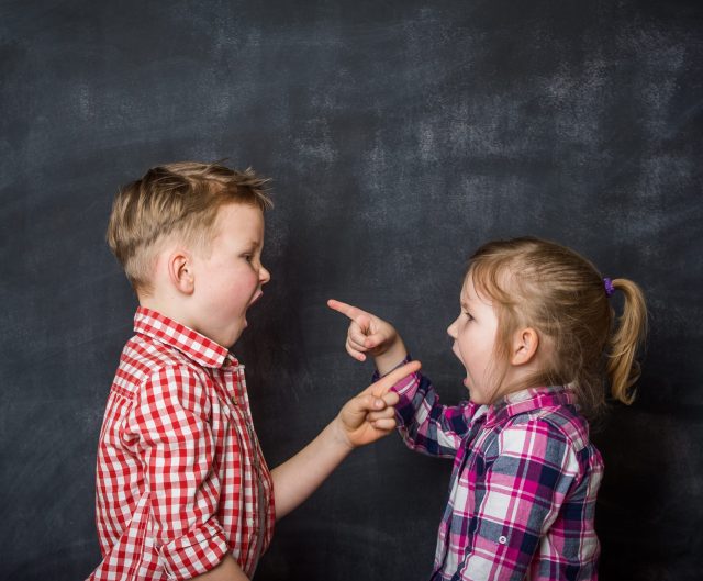 Boy and girl pointing fingers to each other. Raging kids - children shouting to each other against blackboard background. Angry kids.